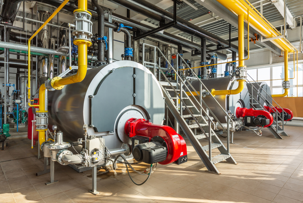 The interior of an well maintained industrial boiler room featuring three large boilers, surrounded by a complex network of pipes, valves, and sensors.